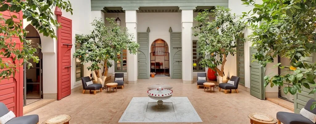 ODM-Where-to-Stay-in-Morocco A typical courtyard in a Moroccan riad with a fountain in the middle, outdoor seating around, and doors leading to private rooms all around.