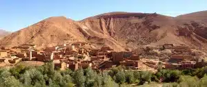 sandstone kasbahs against a vibrant blue sky with green fields and trees surrounding