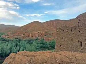 A traditional mud-brick Kasbah featuring intricate geometric patterns under a clear blue Moroccan sky, with greenery in the foreground.