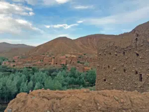 A traditional mud-brick Kasbah featuring intricate geometric patterns under a clear blue Moroccan sky, with greenery in the foreground.