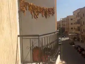 Moroccan balcony in Eid al-Adha with traditional iron railing, displaying drying sheep meat, set against an urban street backdrop showcasing local culture and everyday life in Morocco