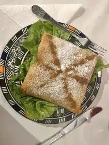 A fried fish fillet served on a green leaf on a plate with traditional Moroccan symbolism.