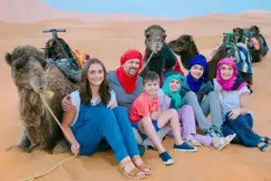 a family of tourists posing for a picture with camels in the dunes of the Sahara desert in Morocco