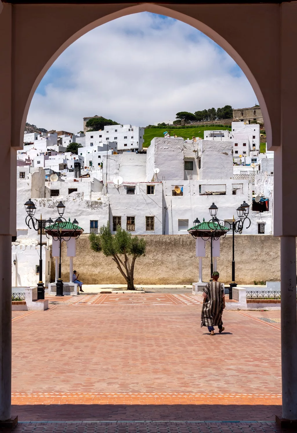 the medina of Tetouan seen through a tall gate with a Moroccan man in the foreground walking towards the medina