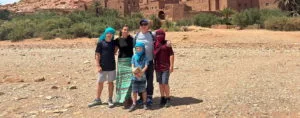 a family of 5 posing for a picture in front of Ait Ben Haddou, wearing several of the clothing articles you'll find in this Morocco packing list