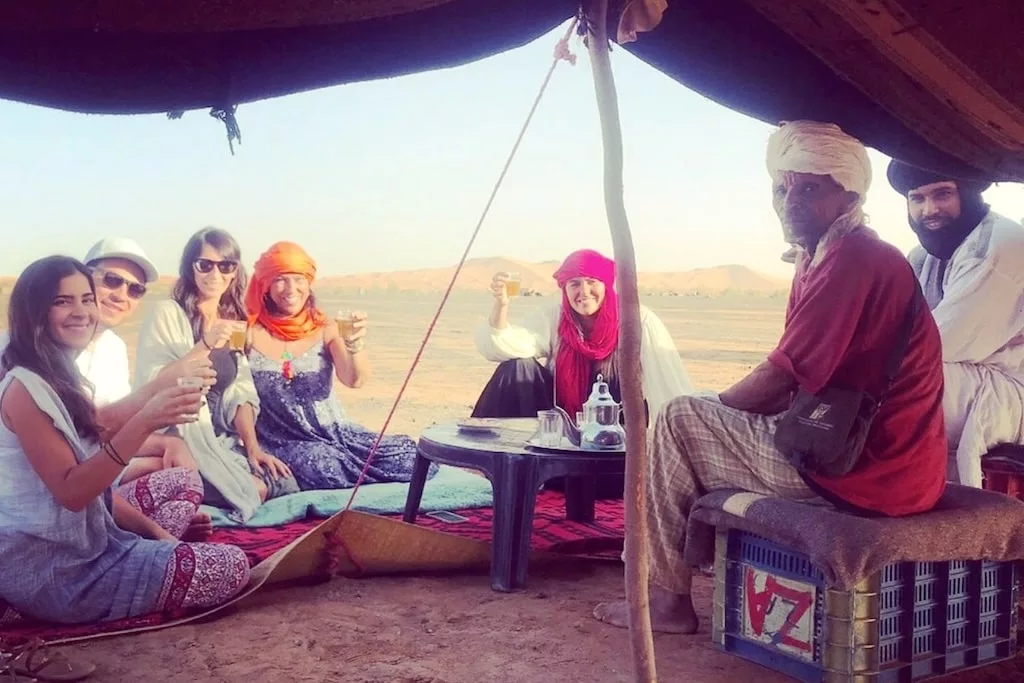 A family of travelers drinking tea with the nomads in the desert.