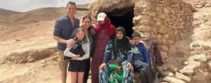 a family of travelers psoing for a picture with a Berber family in front of their dwelling, showcasing the harmonious coexistence of two completely different cultures that responsible tourism in Morocco can lead to