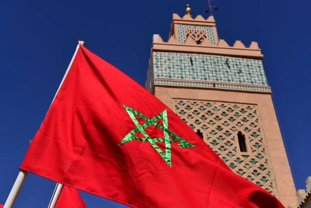 the tower of the Koutoubia Mosque in Marrakech seen behind the red flag of Morocco in the foregorund