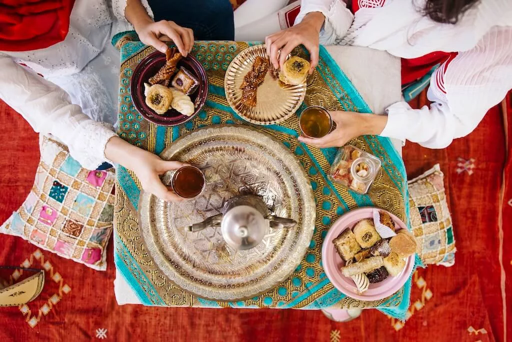 A typical Moroccan festive meal seen from above, with traditional sweets and mint tea being served.