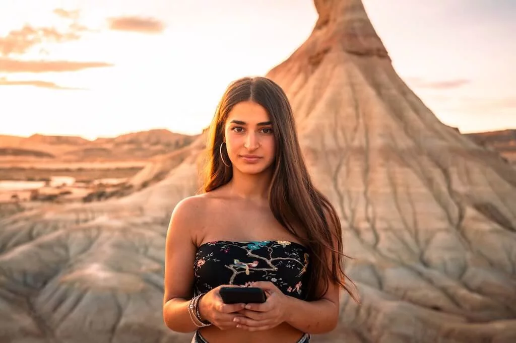 A female traveler standing in the Moroccan desert with her smart phone in her hand.