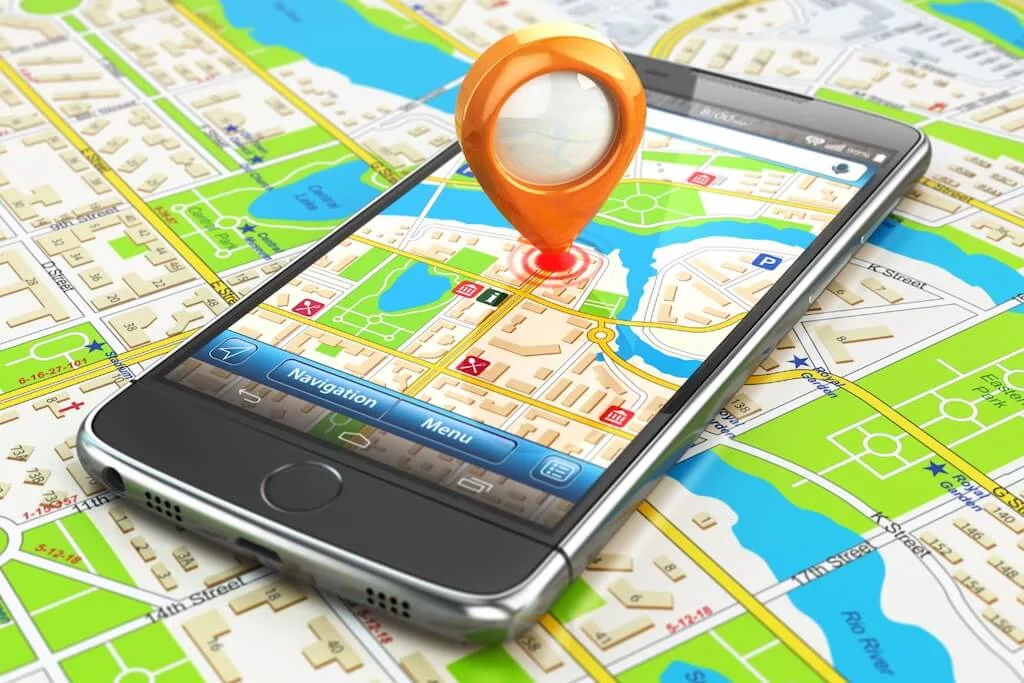 A smart phone lying on top of a map and also showing a Google Map on the display with a location marker in the middle.