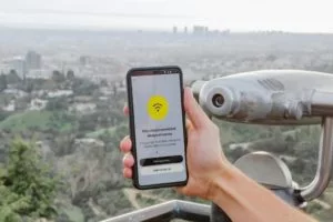 A person holding a smart phone with the WiFi symbol on the display and with a view of a big city in the background.
