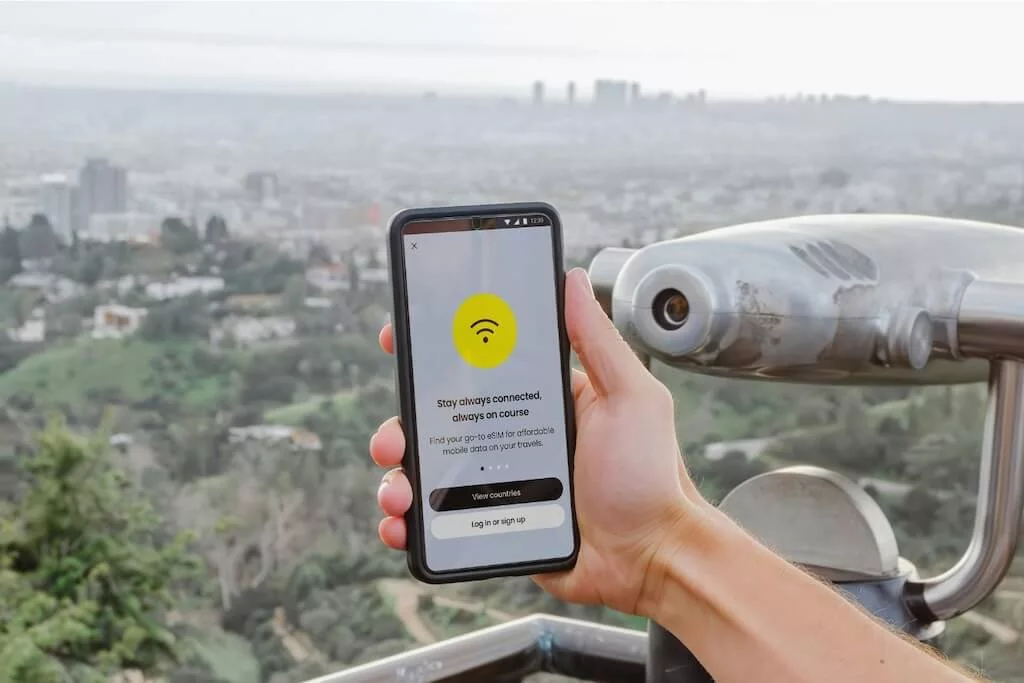 A person holding a smart phone with the WiFi symbol on the display and with a view of a big city in the background.