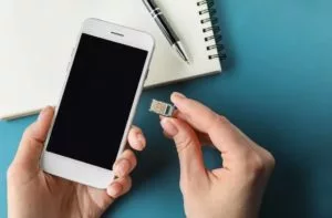 A person holding a smart phone in left hand and a physical Moroccan SIM card in the right hand, ready to start using their phone during their trip to Morocco.