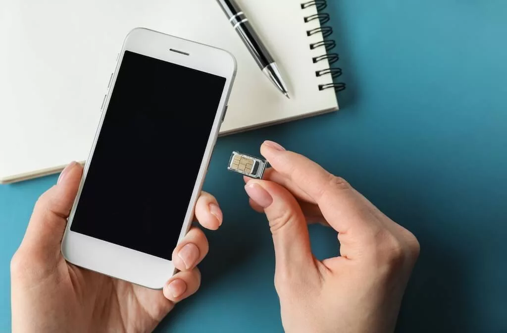 A person holding a smart phone in left hand and a physical Moroccan SIM card in the right hand, ready to start using their phone during their trip to Morocco.