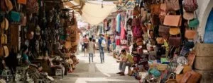 Two tourists walking down a pathway inside the markets in Morocco with handmade Moroccan goods on display on both sides of the alley.