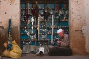 A Moroccan artisan selling silver jewelry and goods in a small opening on the street.