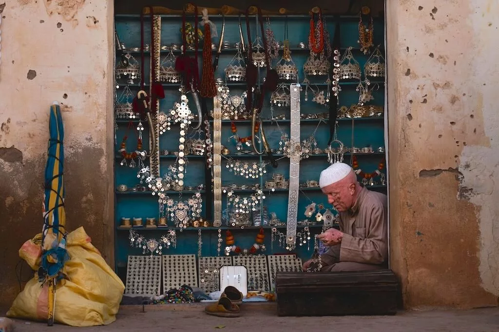 A Moroccan artisan selling silver jewelry and goods in a small opening on the street.