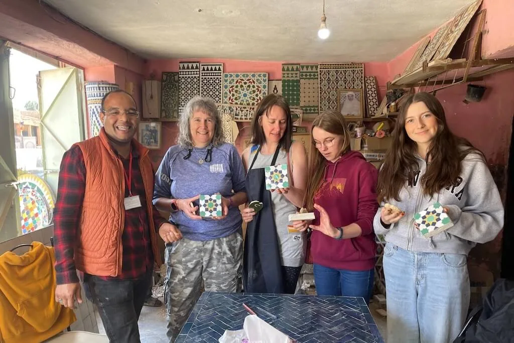 A group of women posing for a picture with Hassan, a local artisan, after a tile workshop.