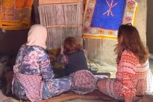 A young girl learning to weave carpets from a local Moroccan woman during a carpet weaving workshop with her mother.