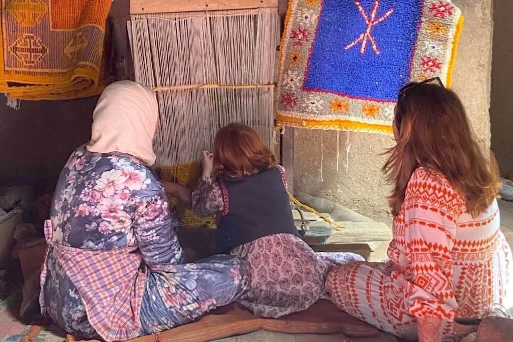 A young girl learning to weave carpets from a local Moroccan woman during a carpet weaving workshop with her mother.