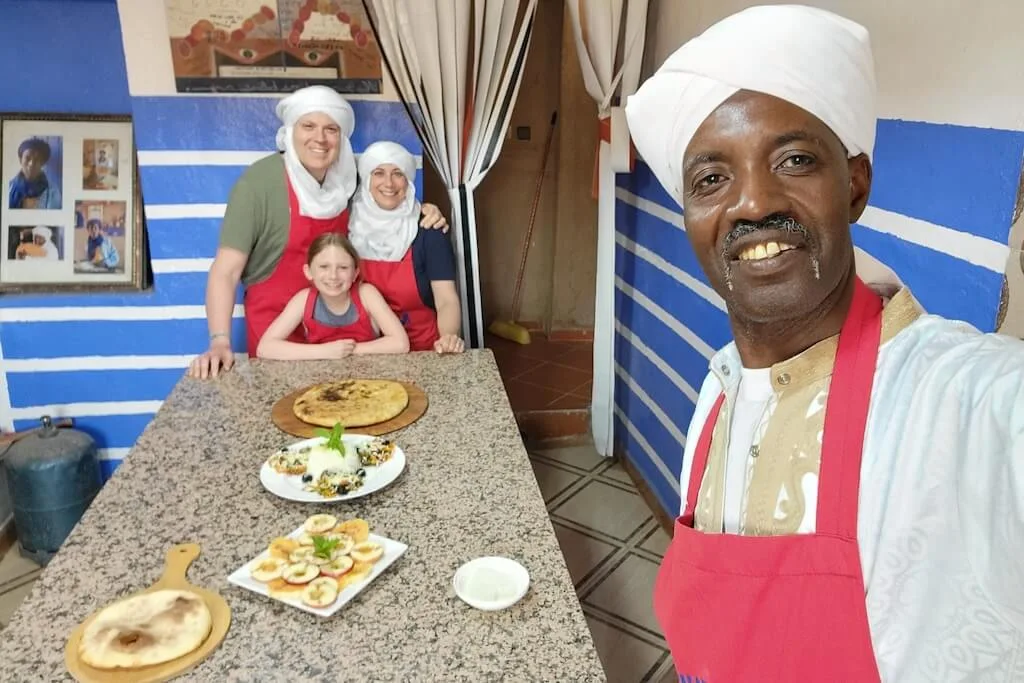 A local chef taking a selfie with a family of travelers after a Moroccan cooking class in Café Nora, where they learned to prepare a Berber pizza.