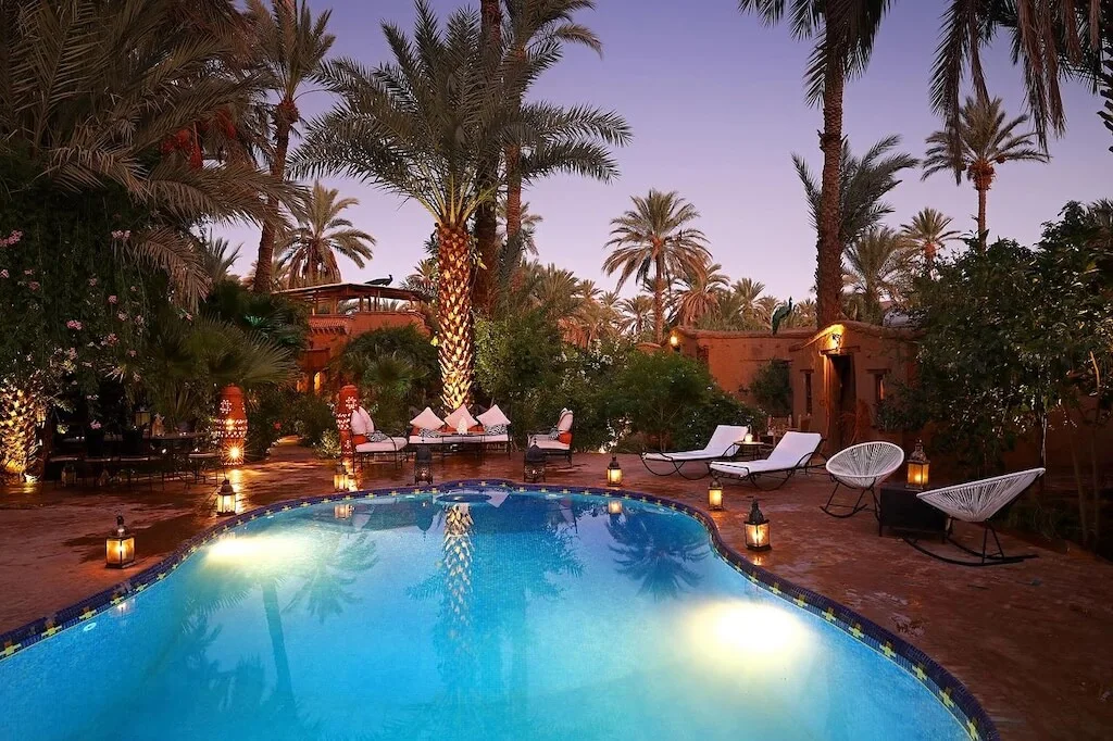 The swimming pool at Bab el Oued at night, with sun beds and chair spread among palm trees.