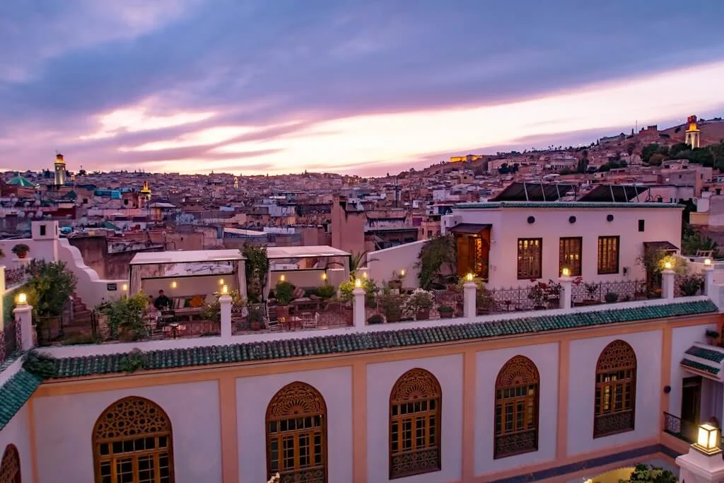 The terrace at Palais Amani at sunset, with tables set for dinner and the view of the city of Fes in the background.