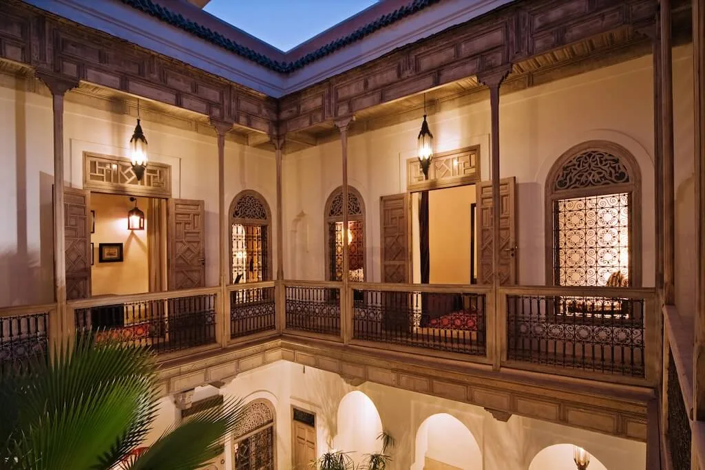 Inside a typical Moroccan riad with a courtyard in the middle and balconies on the second floor with traditional Moroccan decorations.