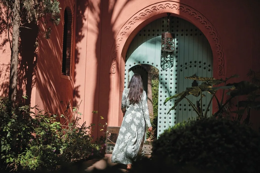 A woman in a long green dress walking through a green gate into a traditional Moroccan riad during her stay in Morocco.