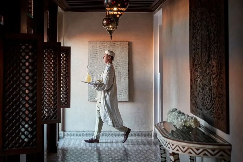 A waiter in a traditional Moroccan clothing carrying a tray with drinks through the decorated halls of Royal Mansour, one of our favorite places to stay in Marrakech.