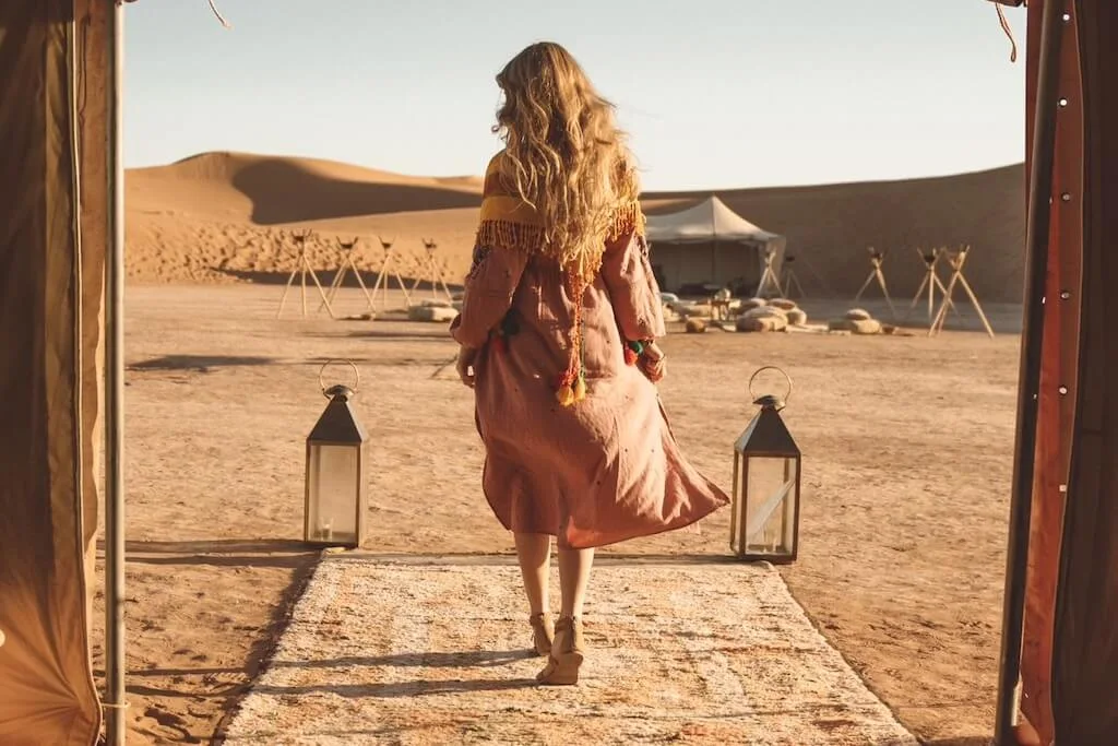 A female traveler walking on a rug out of a ten in a luxury Moroccan desert camp, one of he best places where to stay in Morocco.