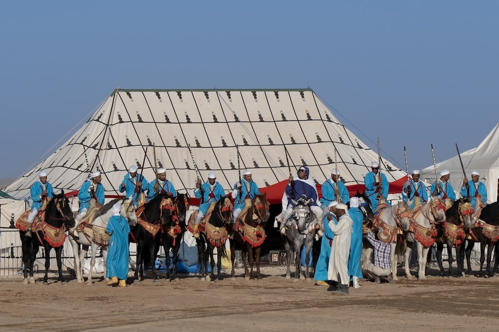 People dressed in traditional blue clothing sitting on decorated horses ready for a celebration of the Moroccan Festival Fantasia