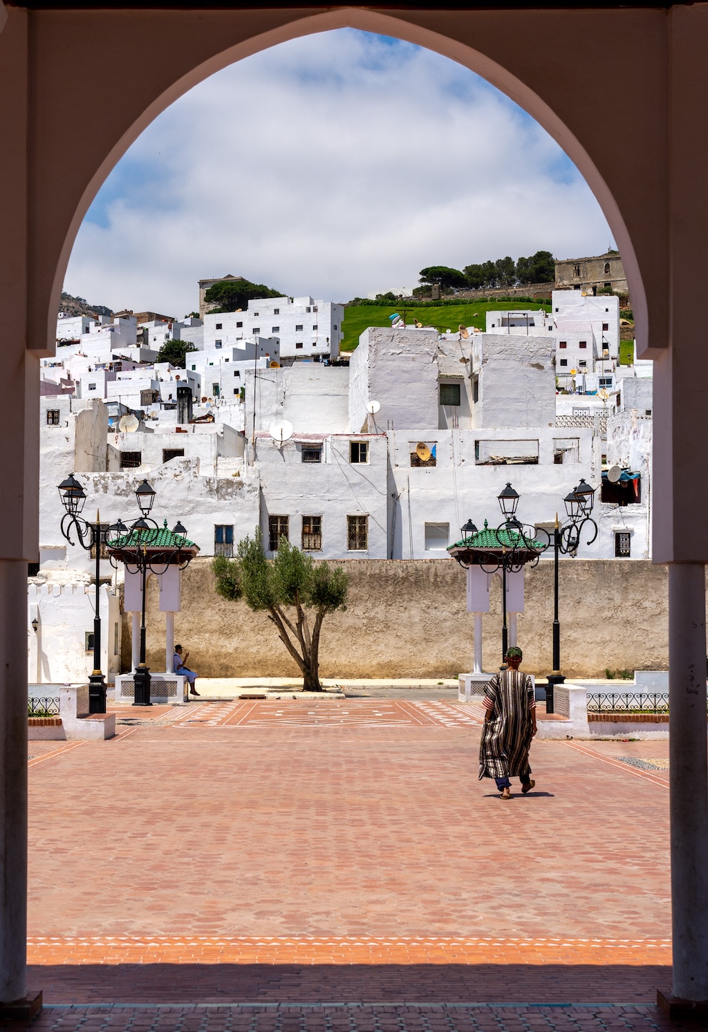 the medina of Tetouan seen through a tall gate with a Moroccan man in the foreground walking towards the medina