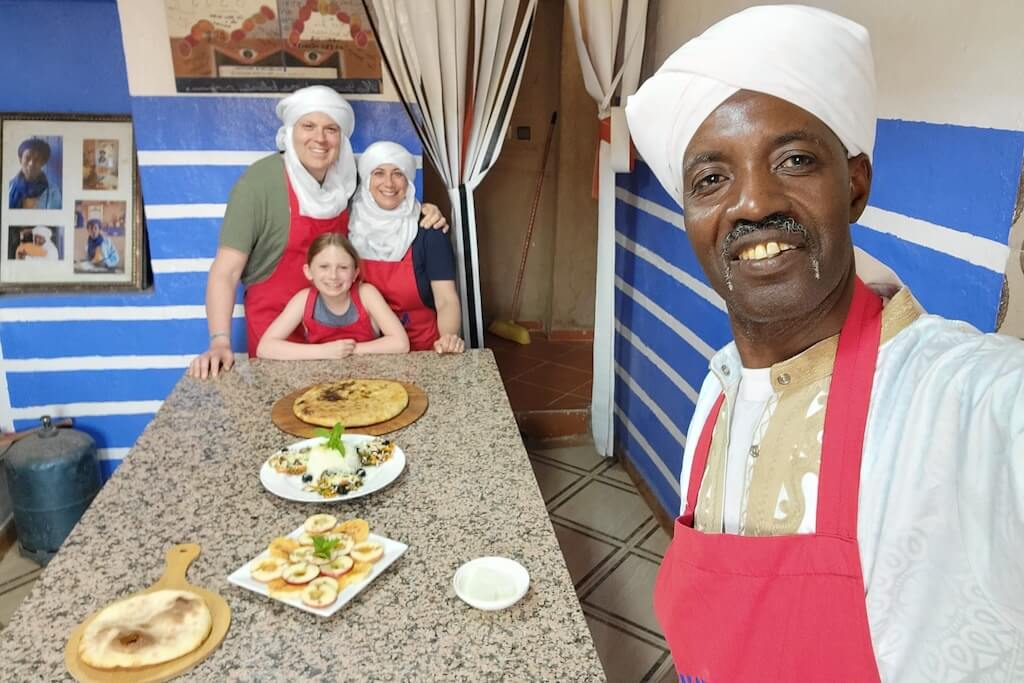 A local chef taking a selfie with a family of travelers after a Moroccan cooking class in Café Nora, where they learned to prepare a Berber pizza.