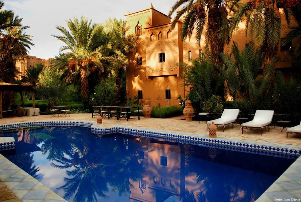 The swimming pool at Kasbah Azul with the view of the medieval kasbah in the background, set among palm trees.