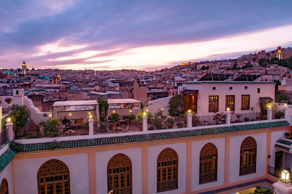 The terrace at Palais Amani at sunset, with tables set for dinner and the view of the city of Fes in the background.