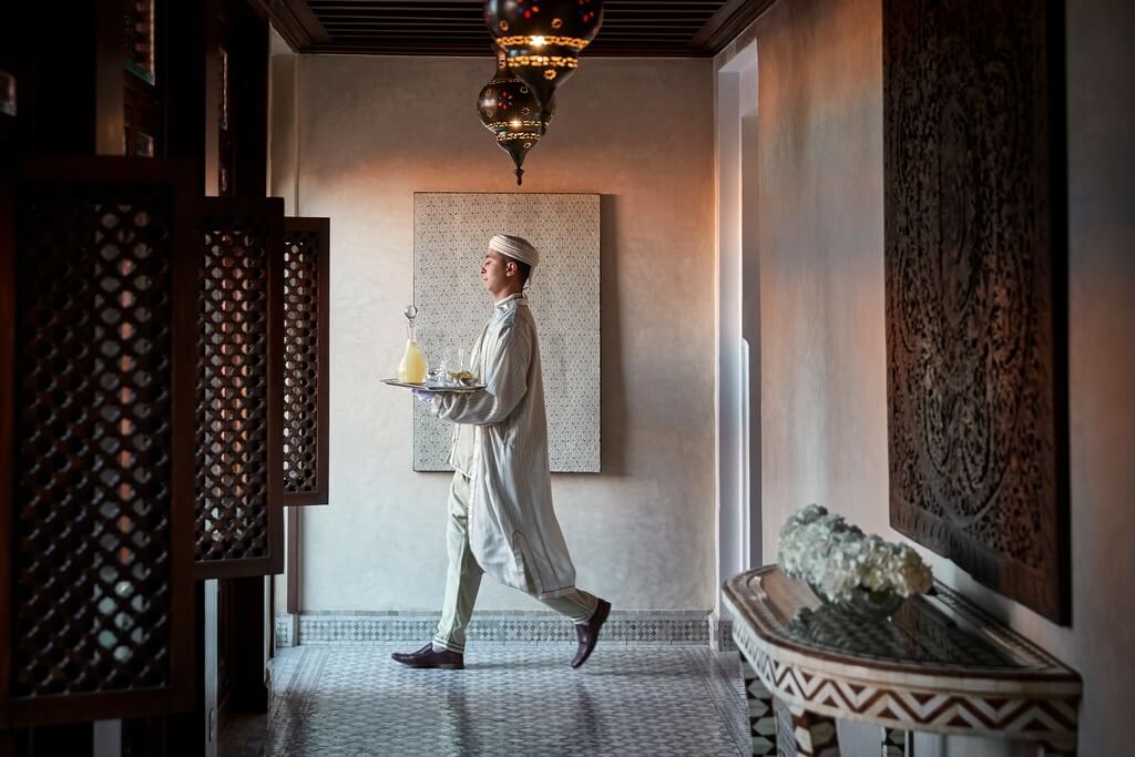 A waiter in a traditional Moroccan clothing carrying a tray with drinks through the decorated halls of Royal Mansour, one of our favorite places to stay in Marrakech.