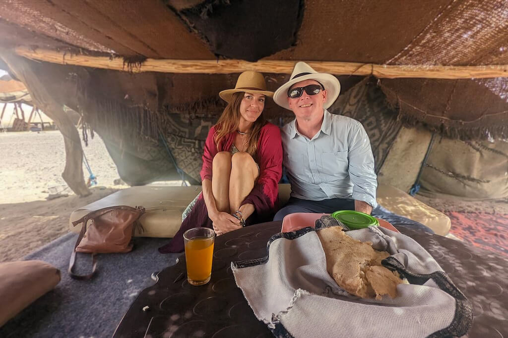 A couple posing for a picture inside a bedouin tent in the Sahara, experiencing the Moroccan idea of romance first hand.