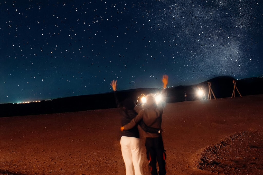 A couple hugging in the Sahara desert under a starry night sky.